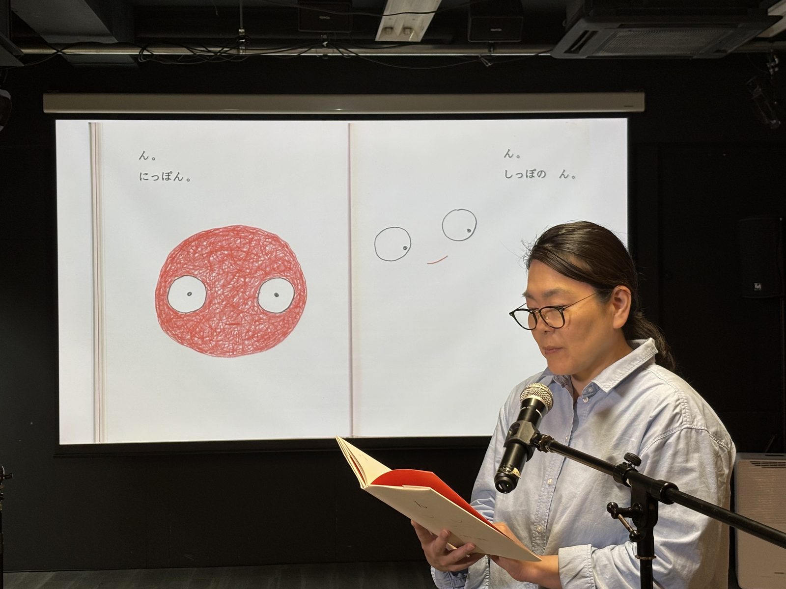 スクリーンに映した絵本を見ながら、マイクの前で朗読する受講生